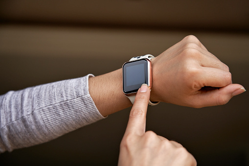 Young woman tries out a generic but modern touch screen smart-watch on his wrist. Using finger to tapping the home screen to make a phone call or send a text message
