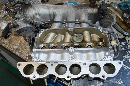 The removed intake manifold of a V6 petrol car engine with broken air dampers lies on the desktop