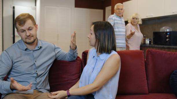 un par de esposas y maridos peleando sentados en casa, hombre y mujer se gritan el uno al otro. conflicto - son in law fotografías e imágenes de stock