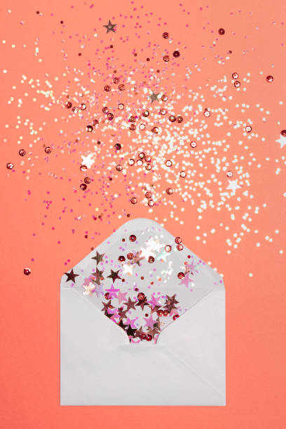 istock Sparkling confetti scattered from envelope on coral background. 1285848328