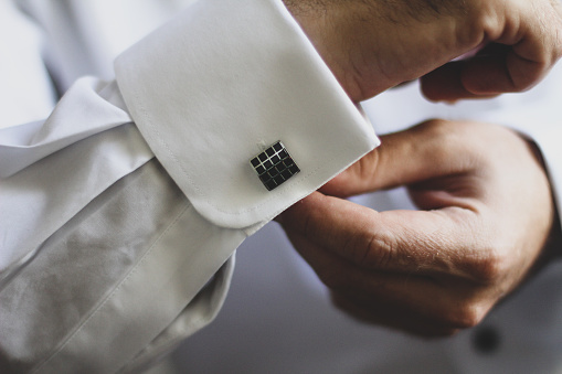 The groom buttoning the cufflinks of his shirt on the wedding day