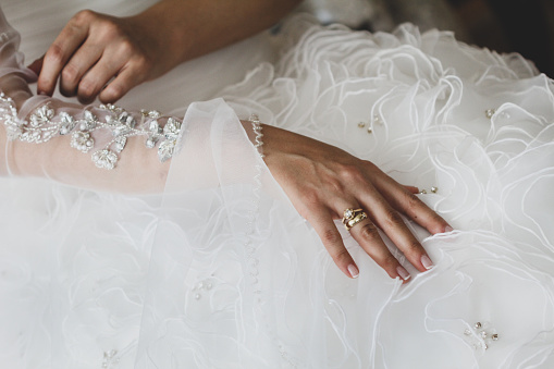 Bride hands wearing diamonds and wedding rings on wedding dress