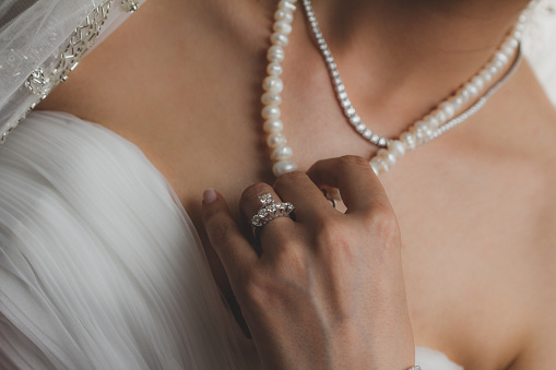 The bride wearing a diamond ring touches the pearl necklace on her neck