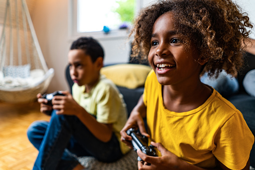 Close-up of young African American girl playing video games with brother at home.
