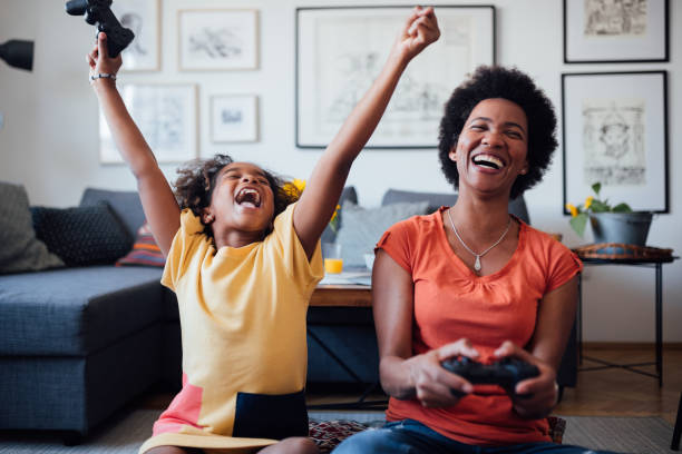 African American mother and daughter having fun at home Single African American mother playing video games with her young daughter at home, competing and enjoying themselves, smiling woman defeat stock pictures, royalty-free photos & images