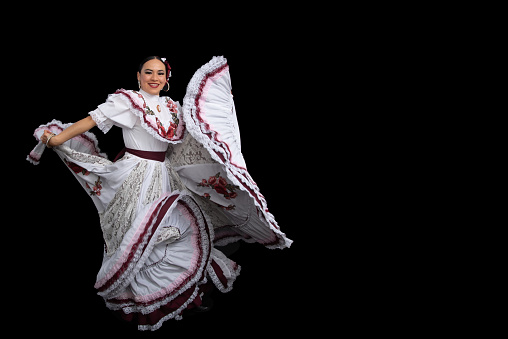 Latin woman dancer wearing dress from Aguascalientes Mexico, black background, with white dress with wine-colored ribbons, moving her skirt and smiling