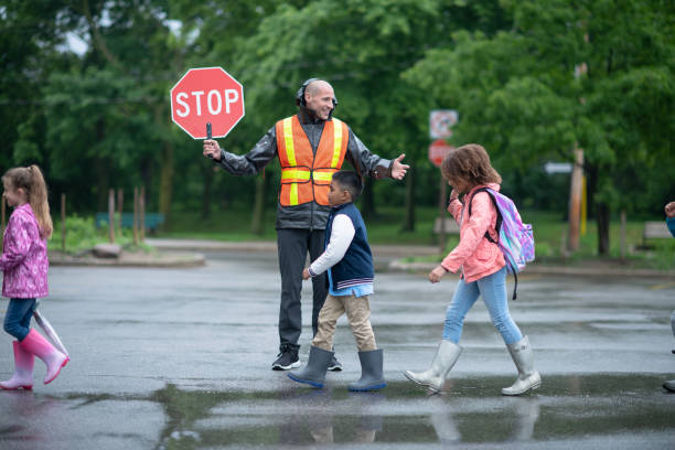 el guardia de cruce ayuda a los niños de la escuela a lo largo - crossing guard fotografías e imágenes de stock