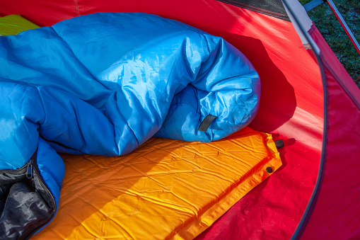 The inside of a red tent with an blue sleeping bag and an orange self-inflating blow-up mattress pad for under his sleeping bag