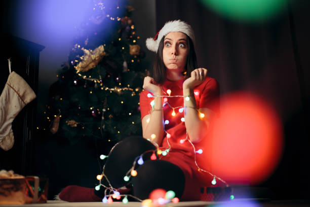 Stressed Woman Tangled in Fairy Lights under Christmas Tree Unhappy girl feeling stuck at home for winter holidays in bounds stock pictures, royalty-free photos & images