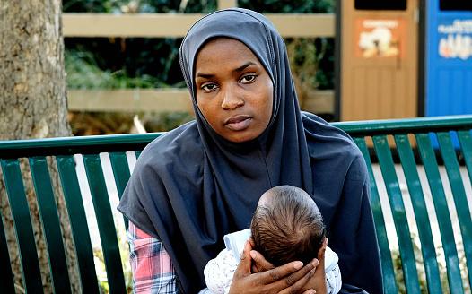 Muslim mother holding her baby sitting in a park bench