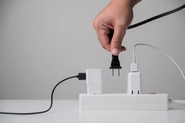 Photo of Hand holding Electric plug put on multiple socket. Electrical equipment, electrical wires and power strips in the house. Earth Hour saving electrical energy.