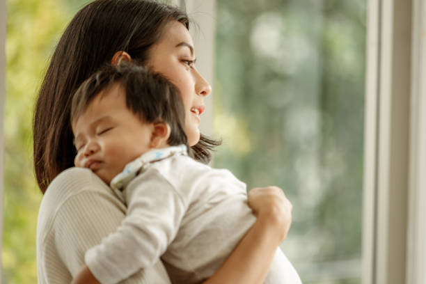 Beautiful young Asian mother holding and hugging her newborn baby in room.single mom motherhood stressful concept. Beautiful young Asian mother holding and hugging her newborn baby in room.single mom motherhood stressful concept. asian nanny stock pictures, royalty-free photos & images