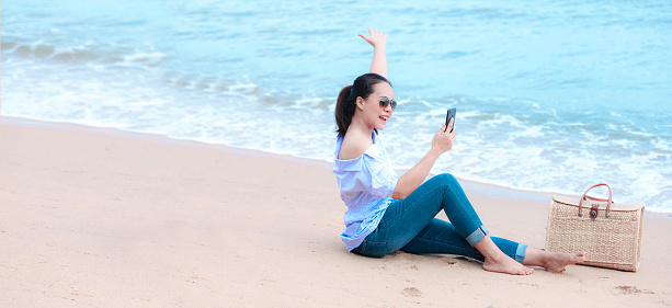 Asian Young woman is feeling happy and freedom, relaxing, sitting on the sand, looking at sea.