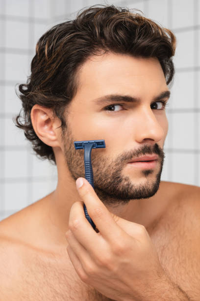 istock Shirtless man looking at camera while shaving in bathroom 1285882108