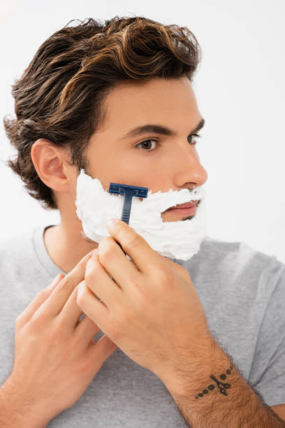 istock Young man with foam on face shaving with razor isolated on grey 1285882131