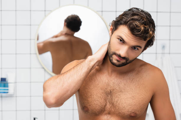 istock Shirtless man touching neck while looking at camera in bathroom 1285882331
