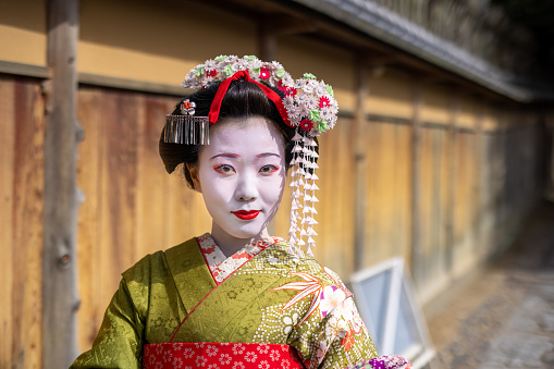 Young female tourist visiting Kyoto in Japan and experiencing Maiko (Geisha in training) makeover. \nWearing traditional Japanese 'Maiko' style kimono with special white face makeup and walking around beautiful city of Kyoto.