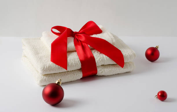istock A stack of cream-colored bath towels on a white background with a red satin ribbon and Christmas balls. Gift concept for New Year and Christmas and copy space. 1285888898