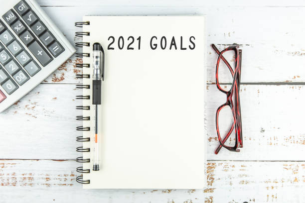 istock Top view of notebook handwriting goals for 2021 year, calculator and eyeglasses on white wooden table 1285889521