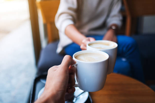 man and woman clinking white coffee mugs in cafe