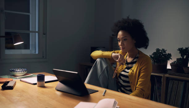 夜遅くに自宅で働く:自宅のオフィスに座ってデジタルタブレットを使った若いアフリカ系アメリカ人女性 - digital tablet businesswoman young women watching ストックフォトと画像