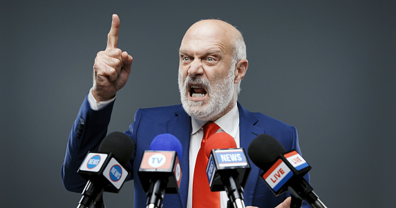 Aggressive politician giving a speech at the press conference, he is pointing his finger and talking in front of the microphones