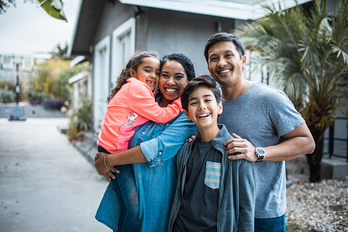 Portrait of four member hispanic family with two children standing in front of their house