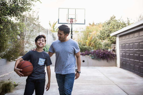 padre e hijo caminando de vuelta dentro después de jugar baloncesto al aire libre - bouncing ball family playing fotografías e imágenes de stock