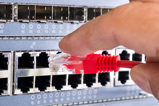 hand of administrator plugging in red patch cable into empty switchboard