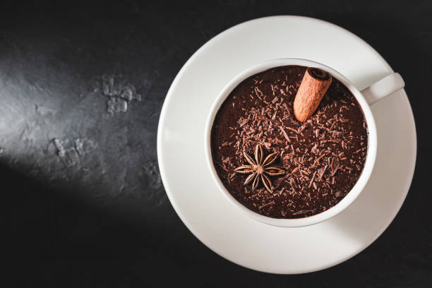 istock Hot chocolate drink in a white cup with cinnamon stick and star anise on textured dark background, top view with copy-space 1285906732