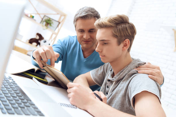 Father helps his son who is doing homework. Troubled teenager tries to study. stock photo