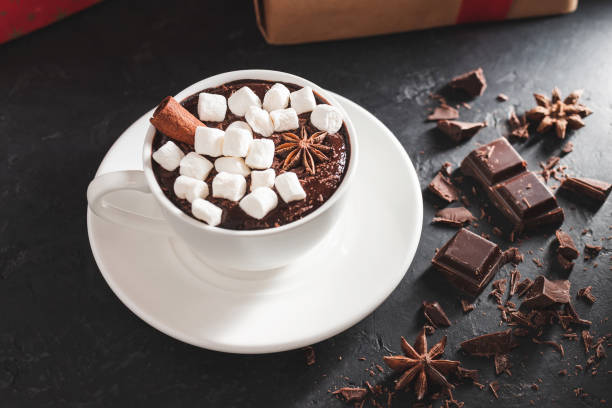 istock Hot chocolate drink in white cup with marshmallow, cinnamon stick, broken chocolate cubes and star anise on dark background 1285906841