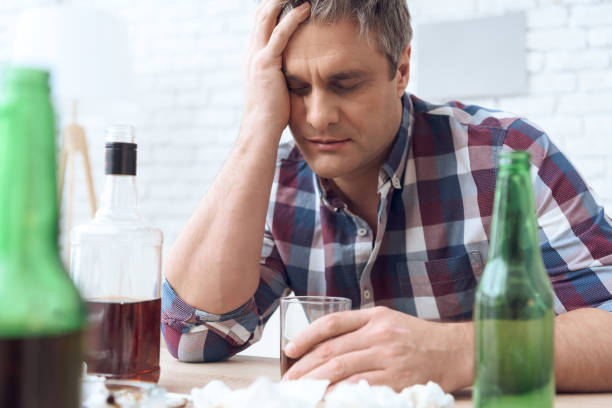 istock Drunk father is sitting at table with glass and bottles, drinking. 1285907947