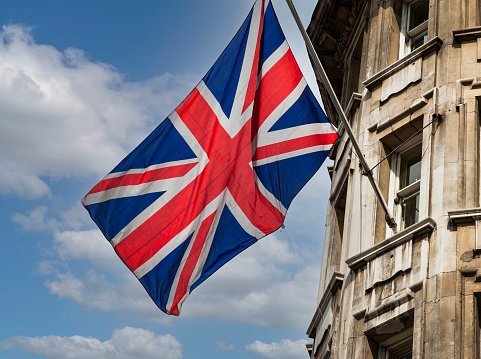 UK flag waving on a building on blue sky background with white clouds.