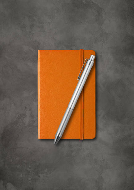 istock Orange closed notebook with a pen on dark concrete background 1285911011