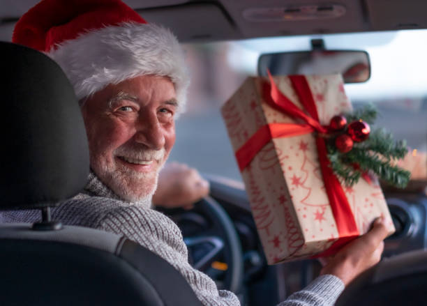 クリスマスプレゼントの宅配の準備ができてサンタの帽子を身に着けている彼の車の中に笑顔の先輩の男。大きな笑顔を浮かべた古いひげを生やした祖父 - one senior man only grandfather portrait old ストックフォトと画像