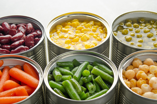Canned carrots, chickpeas, kidney beans, green beans, peas and corn in opened tin cans on kitchen table. Non-perishable foods background