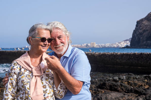istock Romantic senior elderly couple hugging each other lovingly holding hands at the beach - grandparents feel happy with smile faces - relaxed lifestyle enjoying holidays 1285913419