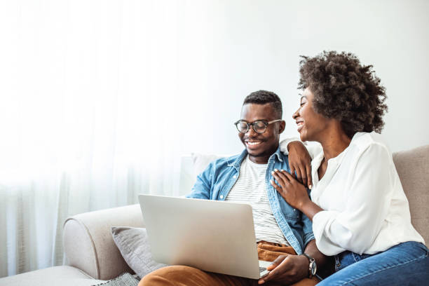 istock Young black couple using laptop sitting on the sofa at home. 1285913879