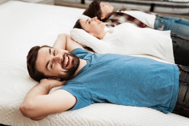 Young happy couple with cute little boy lies on bed in mattress store. stock photo