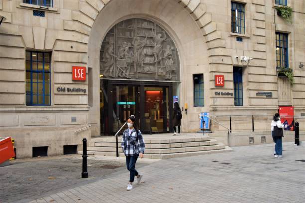 A student with a face mask walks past the LSE Old Building, London School of Economics London, United Kingdom - November 13 2020: A student wearing a protective face mask walks past the LSE Old Building, London School of Economics and Political Science. Universities are permitted to stay open during the second national lockdown in England. university of london photos stock pictures, royalty-free photos & images