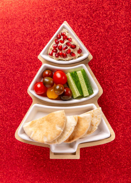 istock Hummus with vegetables and pita served on Christmas tree plate on shiny red  background. Festive holiday snack. Top view. 1285920440