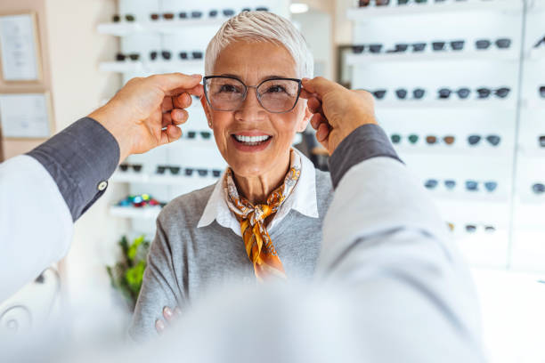 Eye health is fundamental Smiling senior woman trying out new reading glasses at optician office. The doctor is putting on the glasses to see if it fits her. eye exam stock pictures, royalty-free photos & images