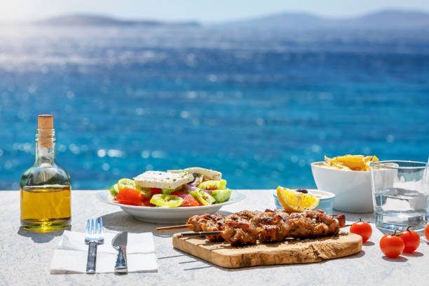 Greek food concept with a farmers salad in front of the Aegean sea Greek food concept with farmers salad and souvlaki skewers in front of the sparkling, blue Aegean sea during summer time mediterranean sea stock pictures, royalty-free photos & images