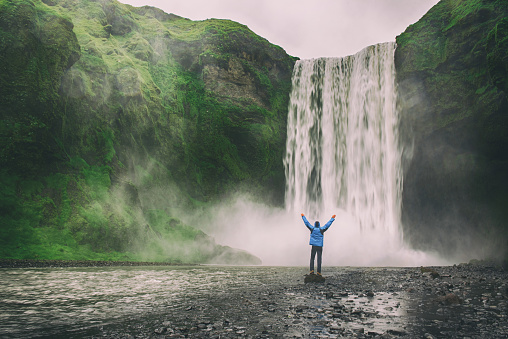 Single man standing near Scogafoss waterfall in Iceland and spread his hands. Travel summer nordic concept.