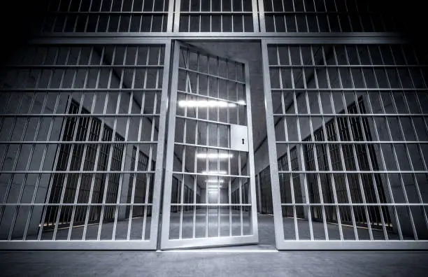 Photo of corridor of a prison with bars and open cell door.
