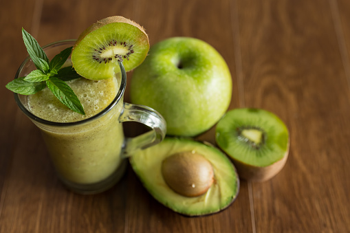 Blended green smoothie with fresh avocado, kiwi and green apple on brown wooden table, detox and dieting concept