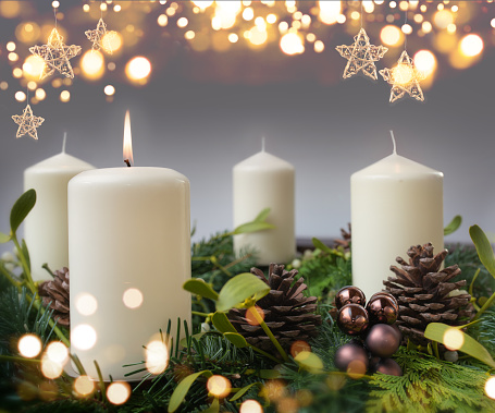 One burning candle in a advent wreath of fir branches with christmas ornament and golden bokeh. Festive background with short depth of field for the christmas season with space for your text.