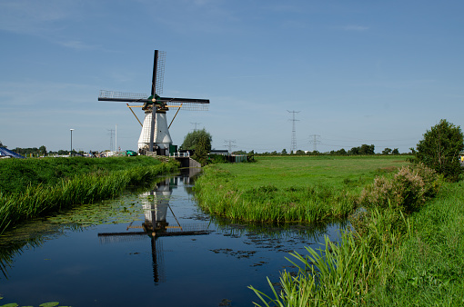 Kinderdijk, The Netherlands, August 2019. Postcard image of Holland: a white windmill is mirrored on the water channel in front of it, creating a pleasant symmetry. Beautiful sunny summer day.