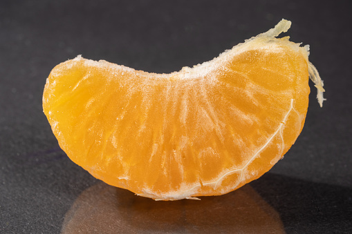 One piece of mandarin close-up. Dark background. Tropical fruit.